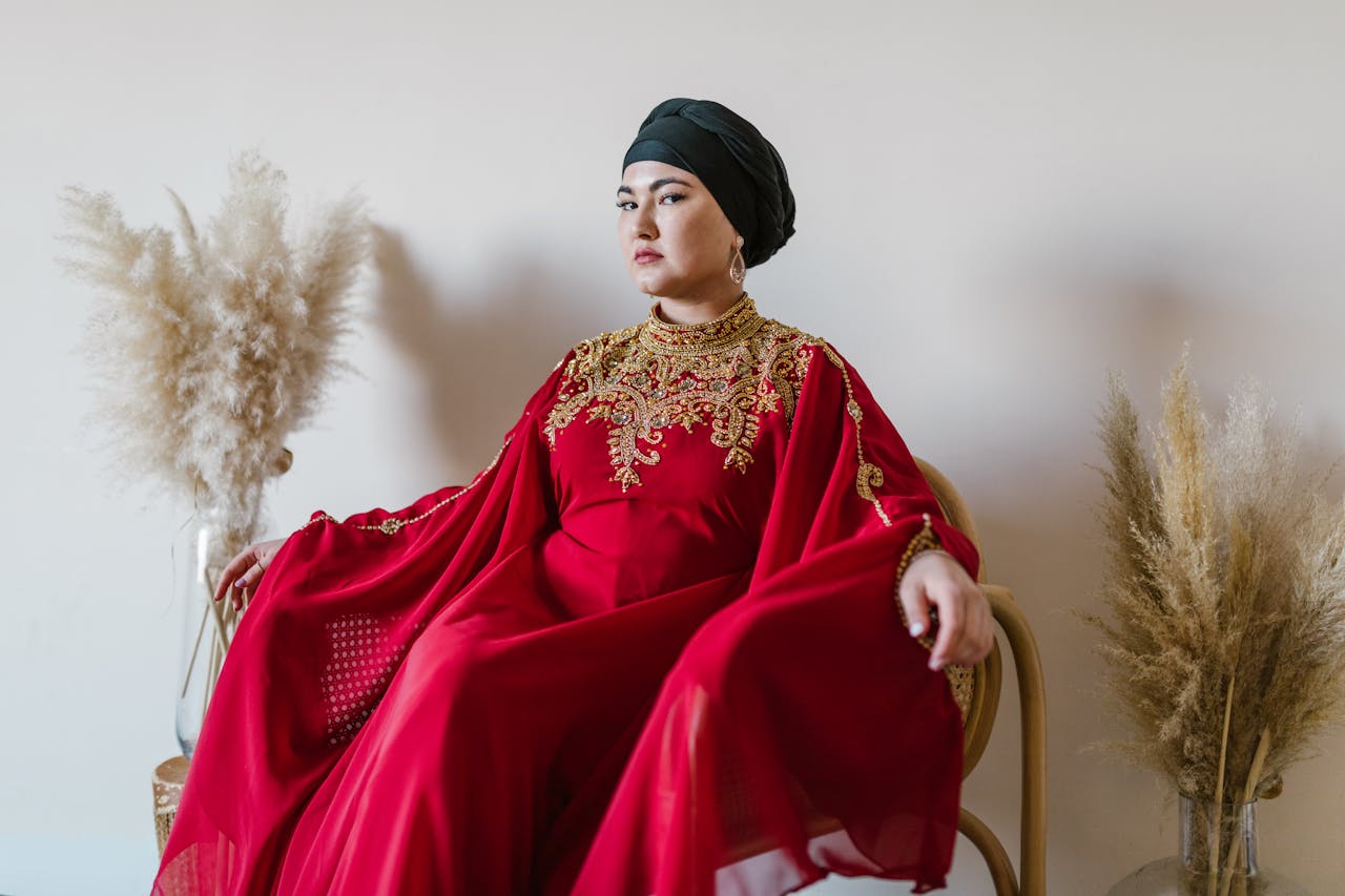 Portrait of a woman in a luxurious red traditional dress sitting elegantly indoors.